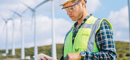 Tecnico posizionato davanti alle turbine eoliche lavorando sul suo tablet
