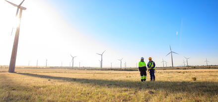 Due ingegneri della Mobil in piedi nel mezzo di un parco eolico. Molteplici turbine eoliche in linea.