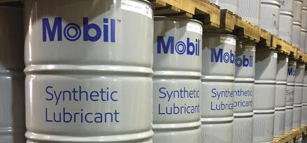 Fusti Mobil™ Synthetic Lubricant impilati su pallet in un corridoio di magazzino ordinato.